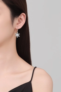 Detail of snowflake drop earring with sparkling zircons worn by a model in silver finish