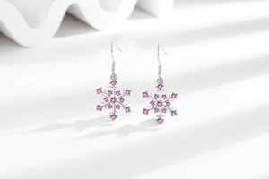 Detailed view of silver snowflake earrings with pink zircons on a white platform