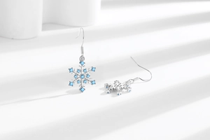 Macro detail of silver snowflake drop earrings with blue crystal accents on white background