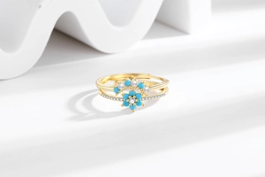 Close-up of gold stacking rings with light blue floral petals and pearl accents