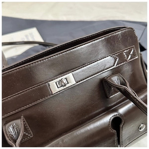 Macro detail of dark brown glossy PU leather bag with silver twist lock and fine stitching
