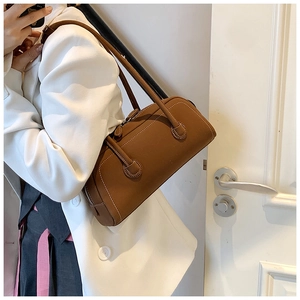 Close-up of brown vintage leather tote with white stitching worn with white suit