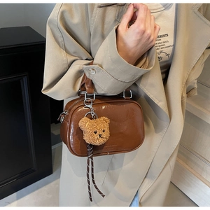 Detail of dark brown glossy bag featuring a cute plush bear charm and vintage brand logo