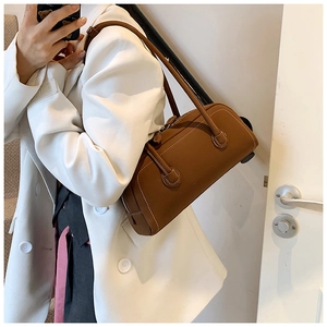 Detail of a brown leather cylinder tote bag with white contrast stitching and zip closure