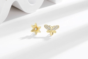 Detail of gold bee and sunflower earrings with zircon accents on minimalist background