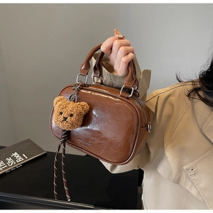 Detail of retro dark brown PU leather Boston bag with teddy bear charm and sleek texture