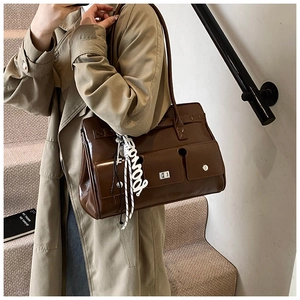 Detail of dark brown polished leather shoulder bag with metallic lock and webbed strap