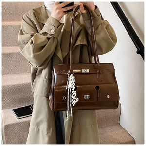 Detail of dark brown leather satchel with metal buckle and letter charm on stairs