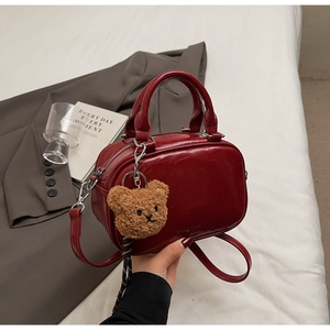 Close-up of shiny red mini Boston bag with a cute brown plush bear charm detail