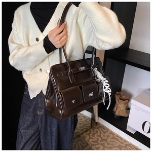 Detailed close-up of dark brown glossy tote bag with dual front pockets and silver buckles