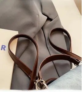 Dettaglio tracolla in pelle PU marrone con anello in metallo su tessuto denim azzurro