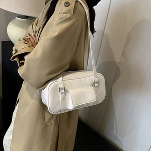 White leather shoulder bag with small front pocket worn by a model in a beige trench coat