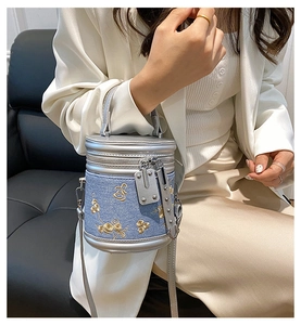 Détail du sac seau en denim bleu clair avec broderie florale et bordure en cuir argenté