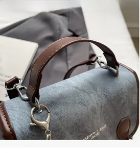 Dettaglio della trama denim azzurra e manico in pelle marrone con anelli in metallo