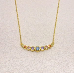 Detail view of gold necklace featuring nine vibrant rainbow gemstones in a curved pendant