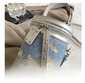 Détail du sac barillet en denim bleu avec broderie florale et bordure en cuir argenté
