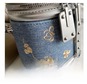 Détail du sac seau en denim bleu avec broderie florale dorée et rivets argentés