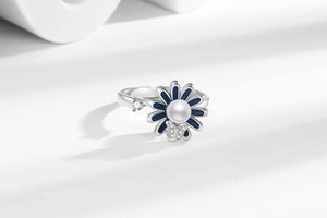 Macro shot of silver ring with blue enamel daisy, pearl center and diamond butterfly