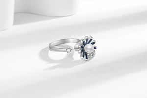Detail view of rotating sunflower ring with blue enamel petals and a white pearl accent