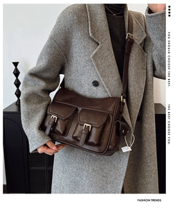 Detail of dark brown retro PU leather shoulder bag with buckle flap pockets on a grey coat