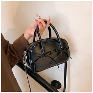Close-up of glossy black patent leather bag with two bow details and silver hardware