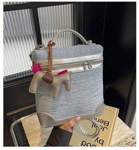 Dettaglio mini borsa in denim blu con finiture argento e ciondolo a cavallo su marmo