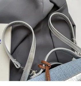 Dettaglio della tracolla in pelle argento e tessuto denim con fibbia su borsa quadrata