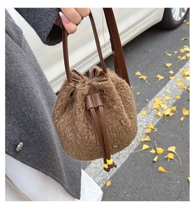 Close-up of brown plush drawstring bucket bag with yellow ball tassels in outdoor setting