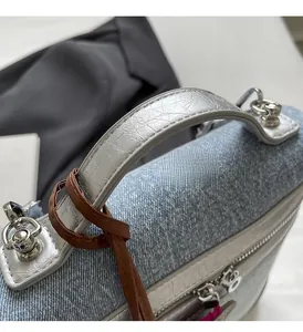 Dettaglio della borsa in denim azzurro con manico in pelle argentata e cordino marrone