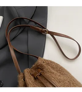 Detail of plush brown drawstring bucket bag with golden eyelets and leather strap