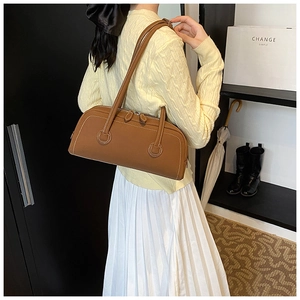 Brown leather Boston tote bag with white contrast stitching shown in a minimalist setting