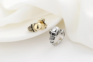 Close-up of gothic skull rings in gold and silver finish on white silk background