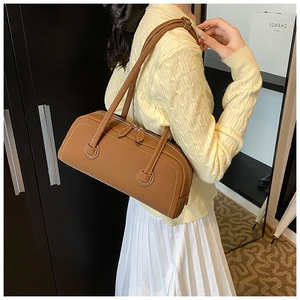 Brown leather tote bag with white stitching shown on shoulder of a model in a knit sweater