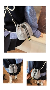 Detail showing grey knit bucket bag with gold lettering and adjustable black strap