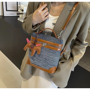 Dettaglio borsa a tracolla in denim blu con finiture in pelle marrone e ciondolo a cavallo