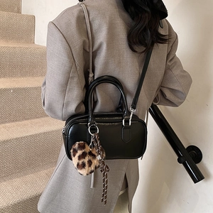 Classic black leather Boston handbag with leopard heart charm worn by model on shoulder