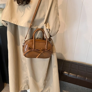 Caramel brown vintage hobo bag with bow decor, shown styled with a beige trench coat