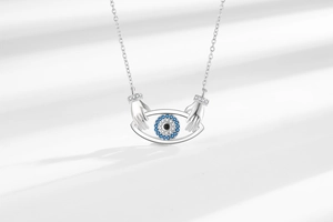 Detail of silver hands holding a blue Evil Eye pendant on a fine link chain necklace