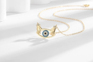 Detailed view of evil eye necklace with hands holding a blue crystal eye pendant