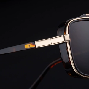 Detail of square amber tortoiseshell sunglasses with gold metal hinges and grey lenses