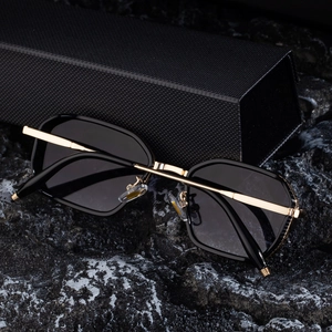 Detail of square black frame sunglasses with gold temples on a textured rock surface