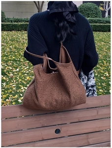 Detailopname van de bruine lamswollen tote bag met leren hengsels op een bank