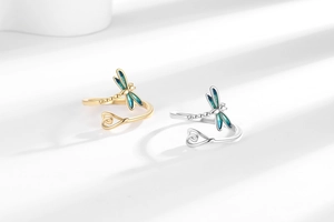 Detail view of gold and silver dragonfly rings with blue gradient enamel wings and heart ends