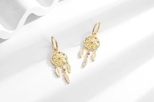 Close-up of golden dreamcatcher earrings with multi-color zircons and feather pendants