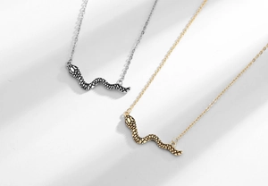 Dettaglio dei ciondoli a serpente oro e argento con trama a scaglie su catenine a O