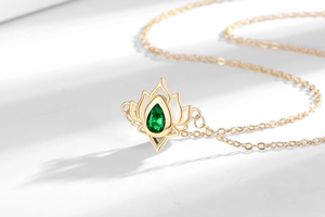 Macro shot of gold lotus pendant with pear-shaped green gemstone on white textured background