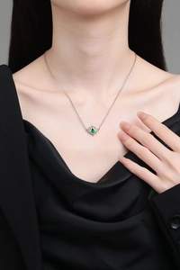 Detailed view of a silver lotus necklace with a green teardrop gemstone on a female model
