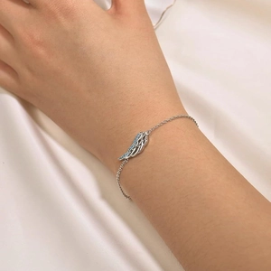 Minimalist silver angel wing bracelet with blue stones on a model's wrist