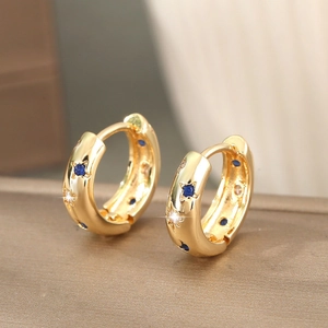 Boucles d'oreilles créoles dorées avec gravures d'étoiles et zircon bleu sur surface texturée
