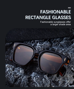 Detailed close-up of square sunglasses with gold metal arrow accents on a rocky texture